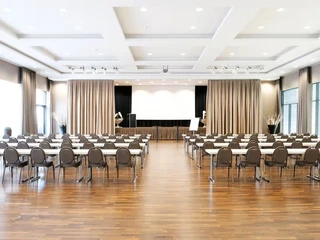 Großer Tagungsraum im Ramada by Wyndham Düsseldorf Ratingen Heller Konferenzraum mit Parkett, weißen Wänden und grauen Vorhängen, bestuhlt für Veranstaltungen.