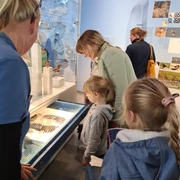 Familienführung im nbz.jpg Eine Gruppe von Menschen, darunter mehrere Kinder, betrachtet aufmerksam eine ausgestellte Federsammlung.