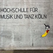 Beethoven Banana by Thomas Baumgärtel Das Bild zeigt ein Straßenkunstwerk von Thomas Baumgärtel an der Fassade der Hochschule für Musik und Tanz Köln. Es stellt eine Banane dar, die in einem stilisierten Porträt Ludwig van Beethoven ähnelt. Die Banane ist in leuchtendem Gelb gemalt, und ihre Oberseite ist so gestaltet, dass sie Beethovens charakteristisches Haar und Gesichtszüge hat.The picture shows a work of street art by Thomas Baumgärtel on the façade of the Cologne University of Music and Dance. It depicts a banana that resembles Ludwig van Beethoven in a stylized portrait. The banana is painted in bright yellow and its upper side is designed to have Beethoven's characteristic hair and facial features.