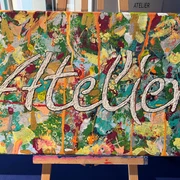 Atelier  Vielseitig gestaltete Leinwand mit dem Schriftzug "Atelier" vor einer Staffelei, farbenreich bemalt.