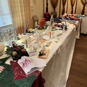 Basar in Godensholt.JPEG Das Bild zeigt einen weihnachtlich dekorierten Verkaufstisch mit Kerzen, kleinen Häuschen, Lichtern und Rezeptheften. Dahinter liegen bunte gestrickte Mützen und Schals auf einem zweiten Tisch.