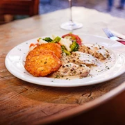 Pfannenhof Rheinisches Gericht mit kleinen Frikadellen, Pfefferrahmsoße, Gemüse und Rösti auf einem Holztisch.