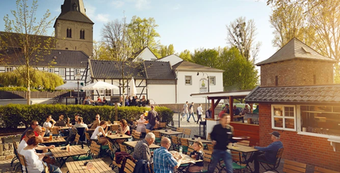 Zollhäuschen Biergarten zur Altstadt Der Biergarten mit Holztischen bietet Sitzplätze im Freien und liegt malerisch vor einer Kirche.