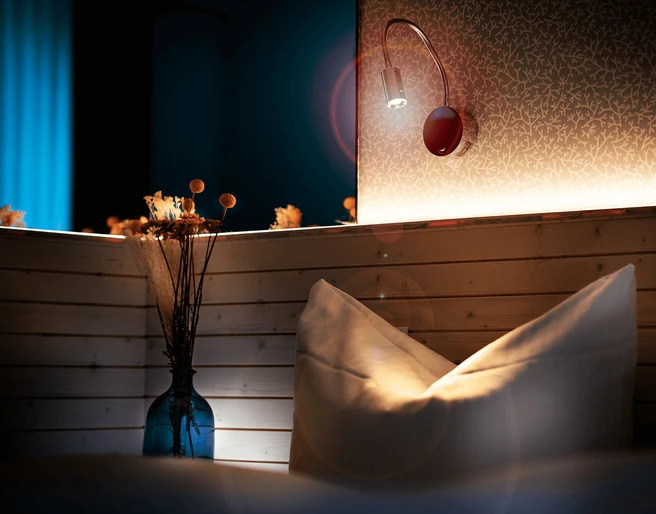 Zimmer im Gästehaus FETTE HENNE in Erkrath Kissen und Lampe in einem stilvoll beleuchteten Gästezimmer mit Holzelementen, dezente Wandtapete.