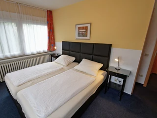 Doppelzimmer im Hotel Wiedenhof in Hilden Zwei Einzelbetten im modernen Hotelzimmer mit Nachttischlampen und einem Fenster mit Vorhängen.