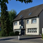 Aussenansicht, Hotel Wiedenhof in Hilden Hotel Wiedenhof in Hilden, zweistöckiges Gebäude mit grauer Fassade und begrüntem Vorplatz.