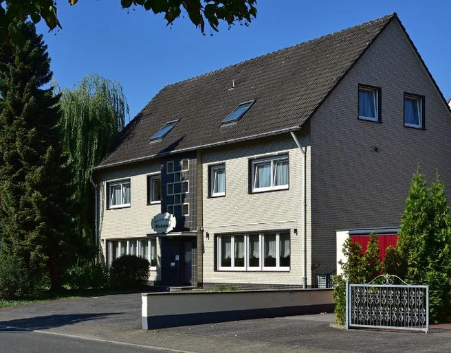 Aussenansicht, Hotel Wiedenhof in Hilden Hotel Wiedenhof in Hilden, zweistöckiges Gebäude mit grauer Fassade und begrüntem Vorplatz.