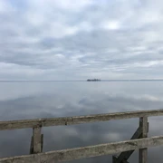 Vogelbeobachtungsturm Winzlar am Steinhuder Meer Holzgeländer vor stiller Gewässerlandschaft mit bewölktem Himmel, im Hintergrund eine kleine Insel.