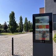 Infostele PS.SPEICHER Digitale Infostele vor dem PS.SPEICHER in Einbeck bei Sonnenschein. Im Hintergrund der Parkplatz des PS.SPEICHER mit Begrünung und Bäumen.