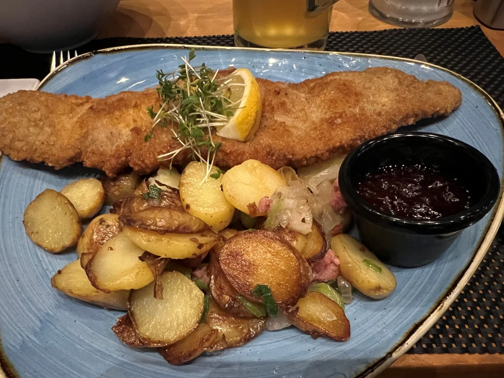 Wiener Schnitzel mit Bratkartoffeln Ein knuspriges Wiener Schnitzel begleitet von goldbraunen Bratkartoffeln und Preiselbeeren.