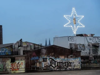 raum13 Das Bild zeigt eine urbane Szene mit Gebäuden im Hintergrund, bedeckt von Graffiti. Ein beleuchteter Stern ragt empor.The picture shows an urban scene with buildings in the background, covered in graffiti. An illuminated star rises up.