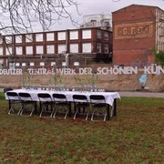 raum13  Eine lange, festlich gedeckte Tafel steht unter freiem Himmel vor einer alten Backsteinfabrik.A long, festively laid table stands in the open air in front of an old brick factory.
