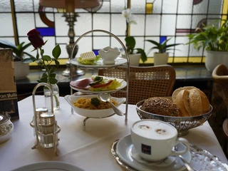 Cafe Wahlen Schön hergerichteter Frühstückstisch mit Brötchen, Cappuccino, Etagere und Vase mit Rose.Beautifully arranged breakfast table with rolls, cappuccino, tray and vase with rose.