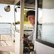 Piwipper Böötchen in Monheim am Rhein Ein älterer Mann in Uniform steht an Bord eines kleinen Flussbootes und blickt auf den Rhein.