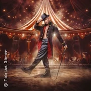 Ein glamouröser Zirkusdirektor im glitzernden Bühnenlicht unter einem schimmernden Zeltdach.