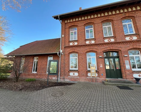 Infoterminal Stolzenau am alten Bahnhof Historisches Backsteingebäude mit Infoterminal, umgeben von einem gepflasterten Vorplatz unter blauem Himmel.