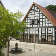Sachsenhagen (10).jpg Fachwerkgebäude säumen einen kleinen, gepflasterten Platz mit einem dekorativen Brunnen im Vordergrund.