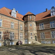 Schloss Landestrost Ein historisches Schloss mit Backsteinfassade und markantem Turm vor strahlend blauem Himmel.