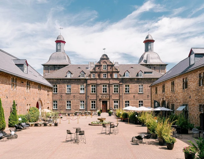 Innenhof vom Schloss Hugenpoet in Essen Historisches Schloss mit Innenhof in Essen, umgeben von Natur, bietet Sitzmöglichkeiten im Freien.