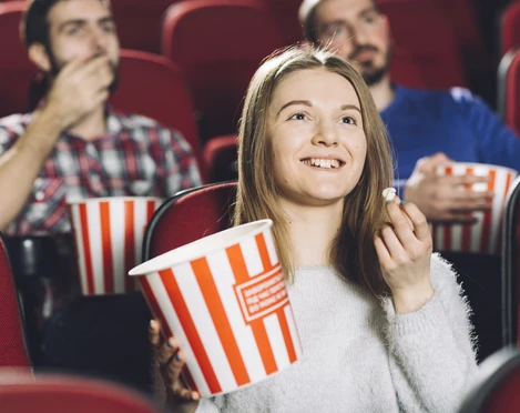 Kino-Sessel-Menschen-Popcorn Junge Frau genießt Popcorn mit Freunden in bequemen, roten Kinosesseln. Alle wirken entspannt.