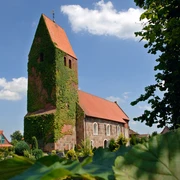 st-johanneskirche Die St.-Johanneskirche mit efeubewachsenem Turm und roten Dächern vor klarblauem Himmel.