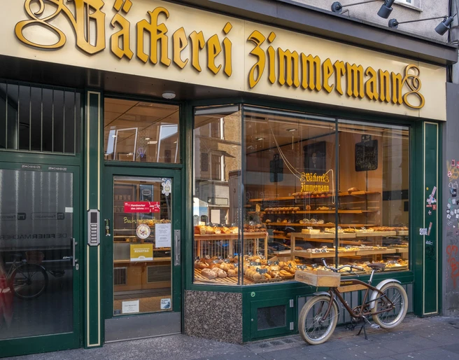 Bakery Zimmermann Außenansicht auf die Bäckerei. Im Schaufenster liegen Backwaren und ein Fahrrad steht davor.Exterior view of the bakery. Baked goods are in the shop window and a bicycle is in front of it.