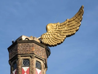 Golden flying car Der historische Wehrturm zeigt ein goldenes Flügelauto auf dem Dach, das sich majestätisch in den blauen Himmel erhebt.The historic defense tower features a golden winged car on the roof, which rises majestically into the blue sky.
