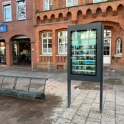 Infoterminal  Ein digitaler Infoterminal in städtischer Umgebung vor Backsteingebäude und Sitzbank.