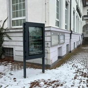 Infoterminal Uchte  Ein Infoterminal steht vor einem schneebedeckten Gehweg neben einem historischen Gebäude mit weißen Wänden.
