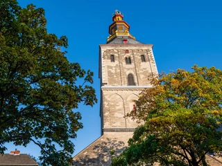Saint Ursula Hoher Kirchturm der Sankt-Ursula-Kirche im Sonnenschein, umgeben von grünen Bäumen.High church tower of St. Ursula's Church in the sunshine, surrounded by green trees.
