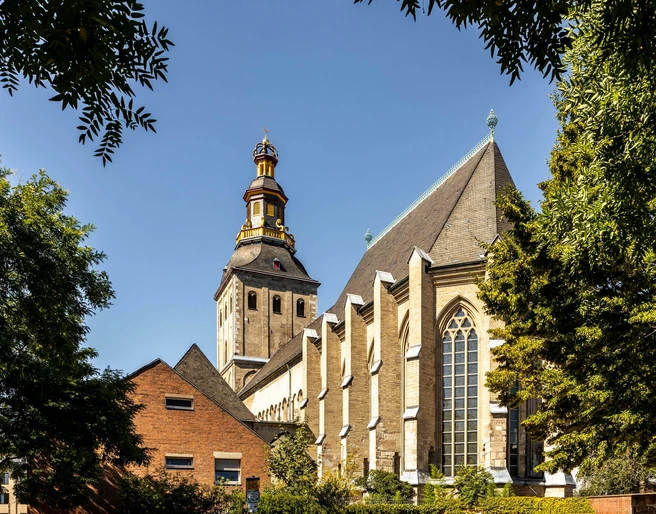 Saint Ursula Sankt Ursula Kirche mit markantem Glockenturm, umgeben von Bäumen, unter klarem Himmel.St. Ursula's Church with its striking bell tower, surrounded by trees, under a clear sky.