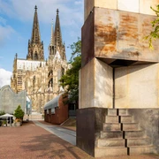 MAALOT Skulptur „MA'ALOT“ von Dani Karavan vor dem Kölner Dom bei sonnigem Himmel.Sculpture "MA'ALOT" by Dani Karavan in front of Cologne Cathedral under a sunny sky.