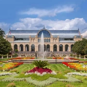 Flora and botanical garden Das Bild zeigt die historische Flora Köln, eine beeindruckende Orangerie mit gläserner Kuppel, eingebettet in farbenprächtige Blumenbeete und einen zentralen Springbrunnen.The picture shows the historic Flora Köln, an impressive orangery with a glass dome, embedded in colorful flowerbeds and a central fountain.