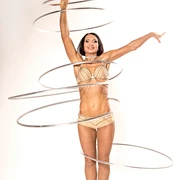 Olena 1.jpg Eine Frau in goldenen Outfits jongliert elegant acht Hula-Hoop-Reifen in einem Studio.