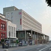 Paderborn Hauptbahnhof mit modernem Empfangsgebäude, Bahnhofsuhren und Werbeplakaten auf der Straße.