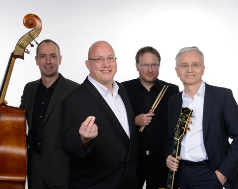 Jörg Hegemann Trio & Rolf Marx Vier Musiker in formeller Kleidung lächeln, mit Klavier, Gitarre, Kontrabass und Schlagzeug.