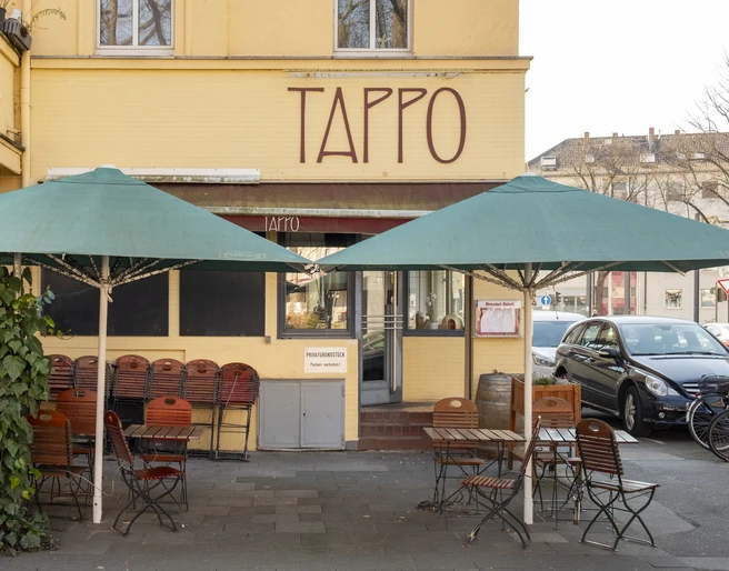 Tappo Außenaufnahme des Restaurants Tappo in Köln mit grünen Sonnenschirmen und leeren Sitzplätzen.Exterior shot of the Tappo restaurant in Cologne with green parasols and empty seats.