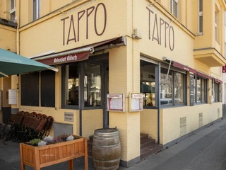 Tappo Gemütliches Restaurant „Tappo“ mit gelber Fassade und großen Fenstern an einer Straßenecke.Cozy "Tappo" restaurant with a yellow façade and large windows on a street corner.