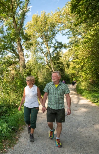 Wandern entlang des Abtskücher Teiches in Heiligenhaus Paar beim Wandern auf einem sonnigen Pfad am Abtskücher Teich, Heiligenhaus, umgeben von Bäumen.