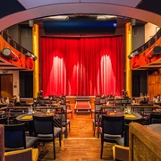 Varietésaal im Krystallpalast Varieté Leipzig - Abendveranstaltungen in Leipzig Blick auf die Bühne mit rotem Vorhang im Varietésaal des Krystallpalast Varieté Leipzig mit zahlreichen Stühlen und Tischen bei heller Beleuchtung, Kultur, Abendveranstaltung