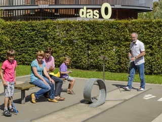 Minigolf im O-Schatz-Park - Freizeit in der Leipzig Region Familie spielt Minigolf, Im Hintergrund die Multifunktionshalle "das O", Freizeit, Tierpark, Familienausflug