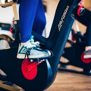 Auf dem Bild sind die Beine einer Person auf einem Fitness-Fahrrad zu sehen, fokussiert auf die Pedale.The picture shows the legs of a person on a fitness bike, focused on the pedals.