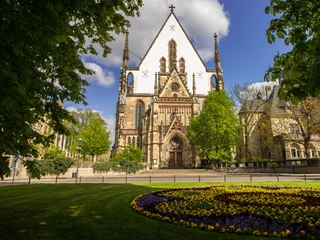 Thomaskirche Leipzig - Musikstadt Leipzig Blick auf die Thomaskirche Leipzig umrahmt von grünen Bäumen, davor eine mit Stiefmütterchen bepflanzte Wiese, Musikstadt Leipzig, Sehenswürdigkeiten