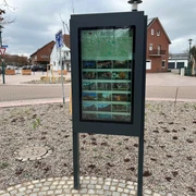 Infoterminal Loccum  Infoterminal mit digitalen Informationen, umgeben von gepflasterten Wegen in einem Vorort.