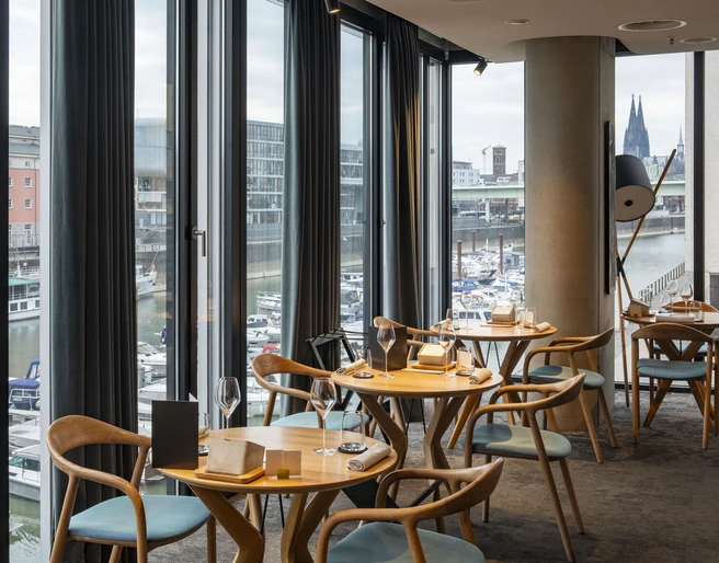 ox&klee Blick in ein stilvolles Restaurant mit großen Fensterfronten. Im Hintergrund Hafen und Domspitzen.View into a stylish restaurant with large window fronts. Harbor and cathedral spires in the background.