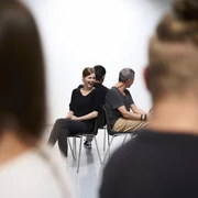 Workshop Team IMPROve Menschen auf Stühlen, Rücken an Rücken, im Dialog. Frau lächelnd, entspannte Gesprächsatmosphäre.