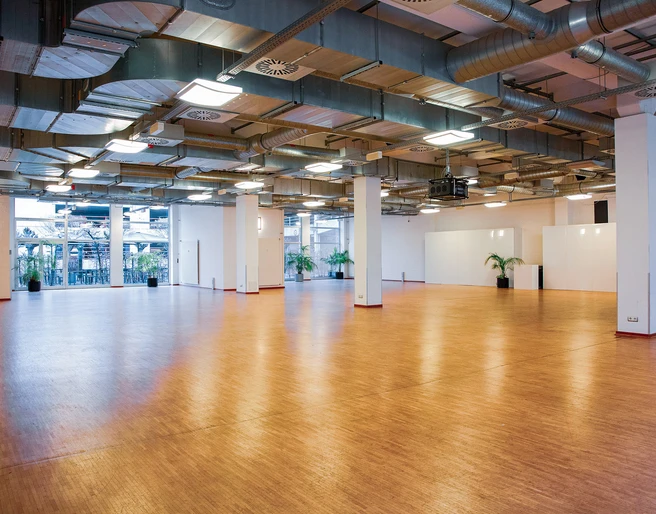 Titelbild (Schlossallee).jpg Großer, leerer Veranstaltungsraum mit Holzfußboden und modernen, industriellen Deckenstrukturen.Large, empty event room with wooden flooring and modern, industrial ceiling structures.