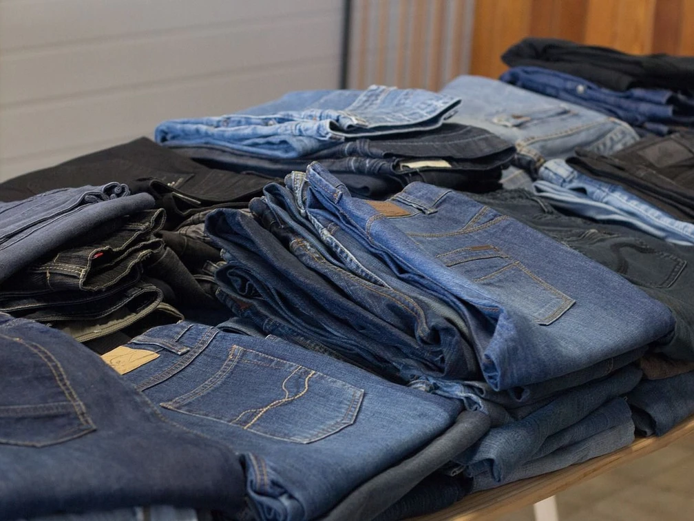 Verschiedene Jeanshosen liegen gestapelt und nebeneinander auf einem Tisch.