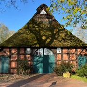 Haus auf der Wurth Fachwerkhaus mit Reetdach und grüner Tür, umgeben von Bäumen, in frühlingshafter Landschaft.