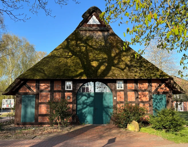 Haus auf der Wurth Fachwerkhaus mit Reetdach und grüner Tür, umgeben von Bäumen, in frühlingshafter Landschaft.